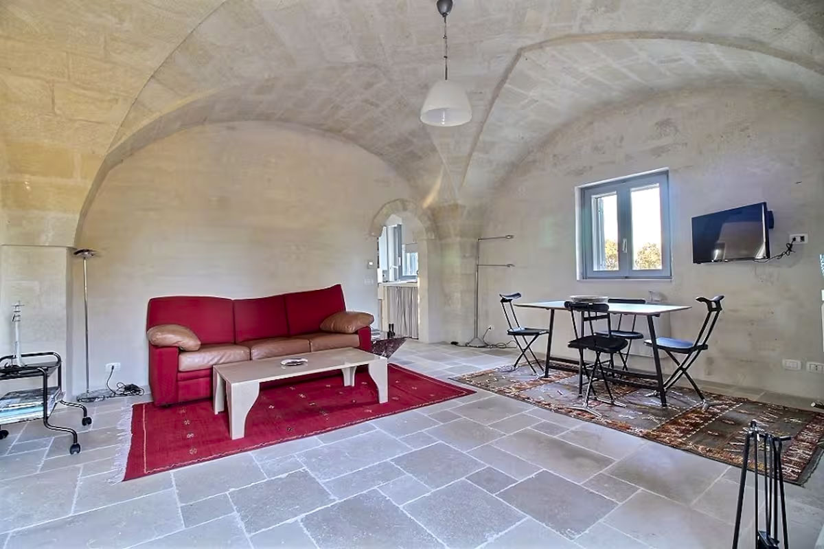 Living room view focusing on the red sofa, dining table, and arched entryway leading to the kitchenette area.