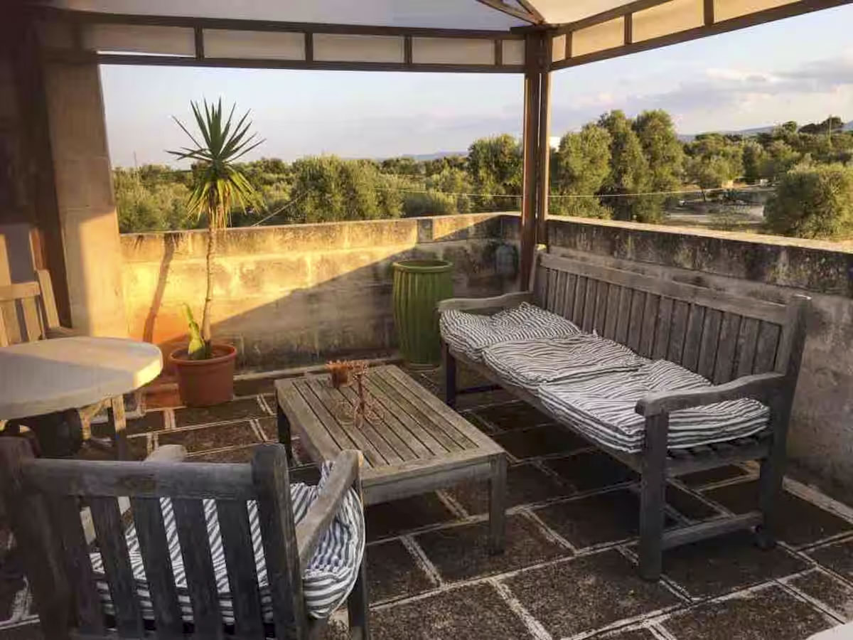 Shaded seating area on the rooftop terrace under a pergola, featuring wooden outdoor furniture and cushions, overlooking the landscape.