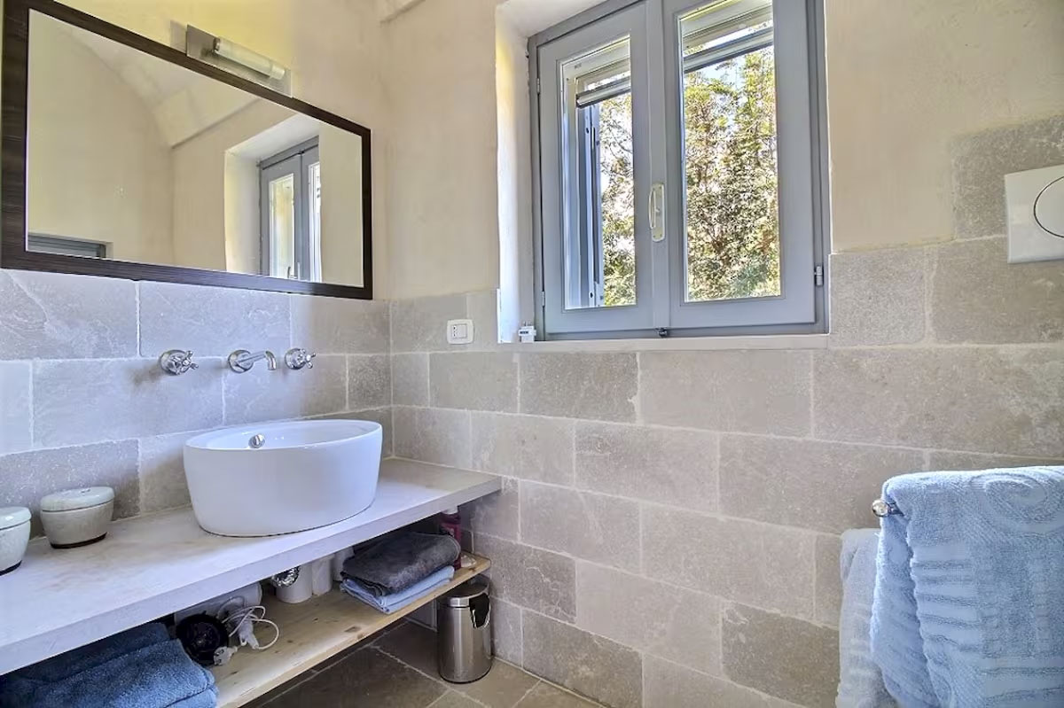 Modern bathroom in Agriturismo apartment with stone block tiling, vessel sink, and large mirror.