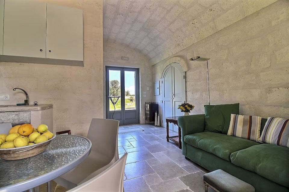 View of the compact kitchen and green sofa lounge area with entry door to the exterior, Masseria apartment.