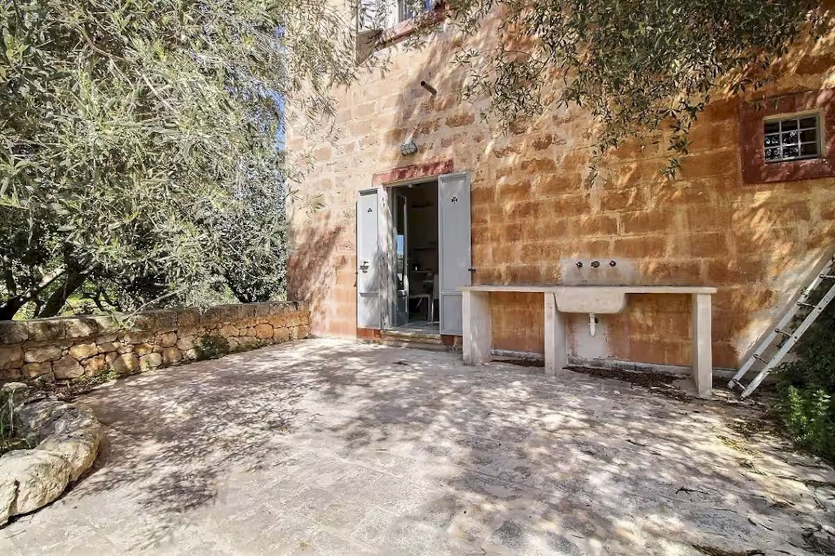 Private patio and garden of Agriturismo San Virgilio apartment with olive tree, stone walls, and rustic sink.