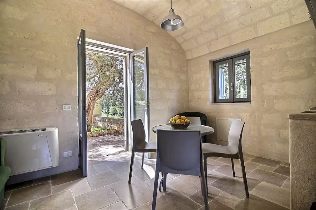 Dining area looking out to the private garden patio and olive tree through open doors, Masseria apartment.