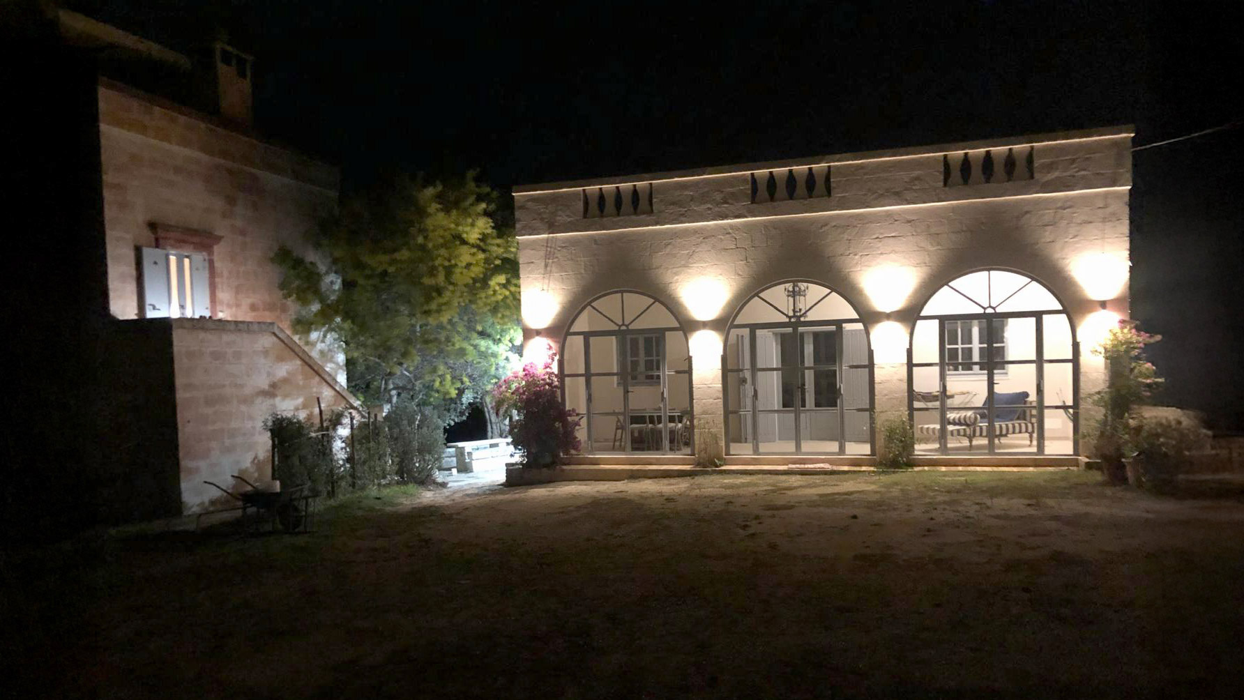 The Agriturismo San Virgilio courtyard at night, illuminated by warm uplighting on the traditional Masseria and the restored arched farmer's house.