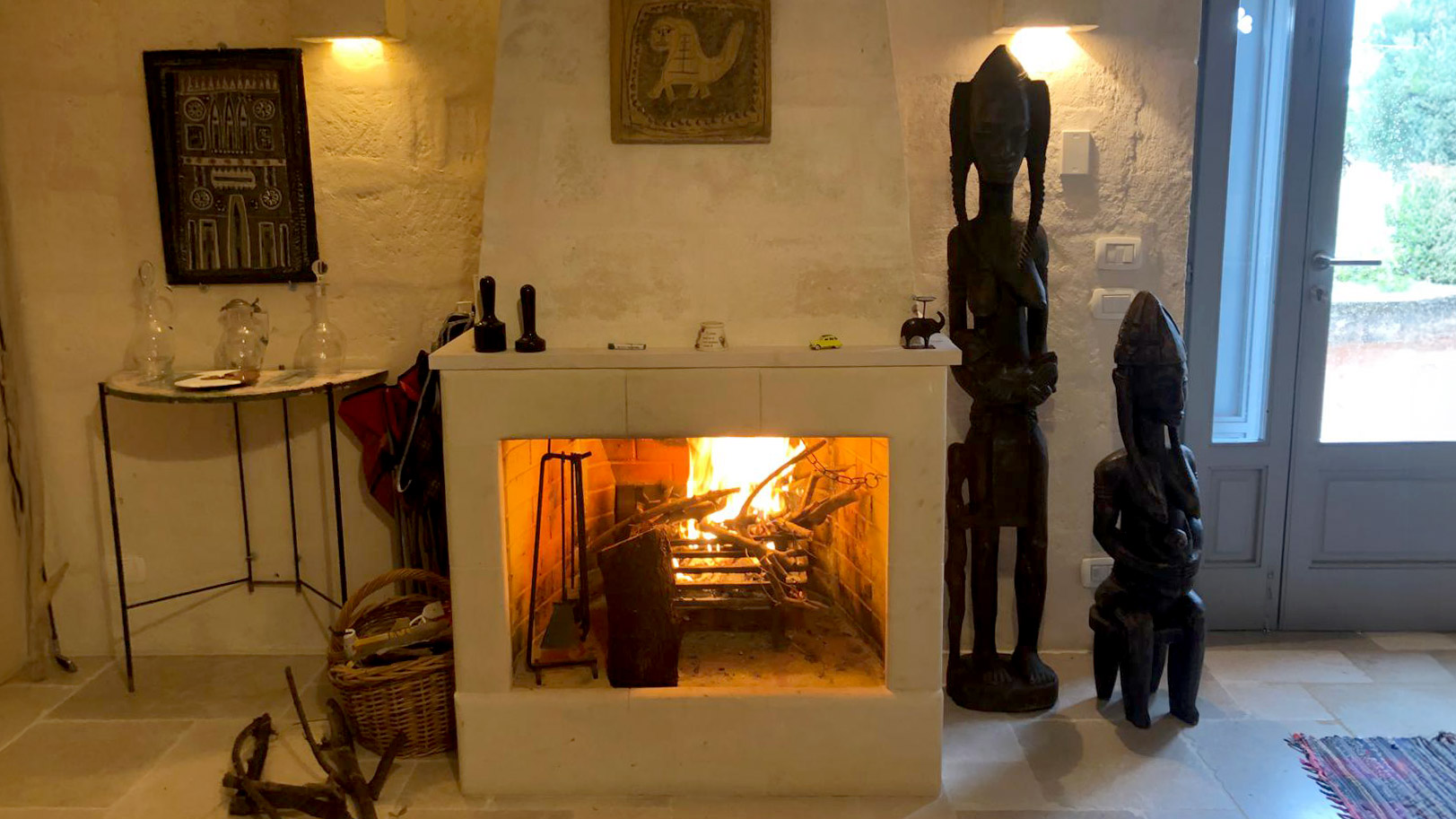 Cheminée chaleureuse avec murs en pierre traditionnels et sculptures d'art africain dans le salon du domaine San Virgilio dans les Pouilles